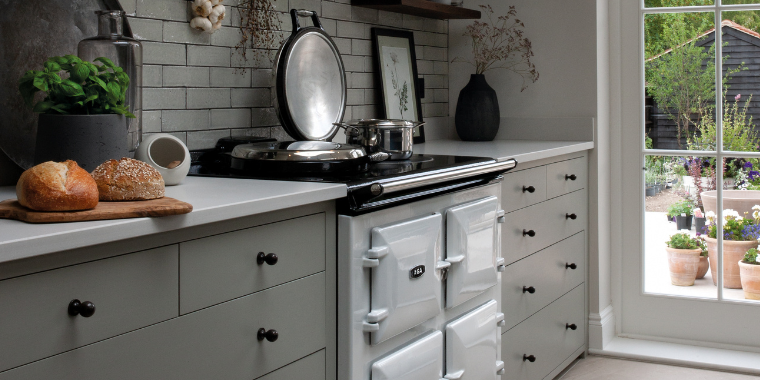 Moderne Landhausküche mit weißem Herd und frischem Brot auf der Arbeitsplatte Stilvolle Küche im Landhausstil mit weißem Kochherd, Backwaren auf einem Holzbrett und Blick auf den Garten durch eine große Fenstertür