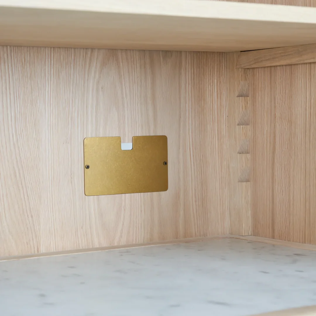Innenansicht eines Holzschranks mit Messing-Kabeldurchlassabdeckung und Marmorablage – verdeckte Kabelführung für aufgeräumte Einrichtung
