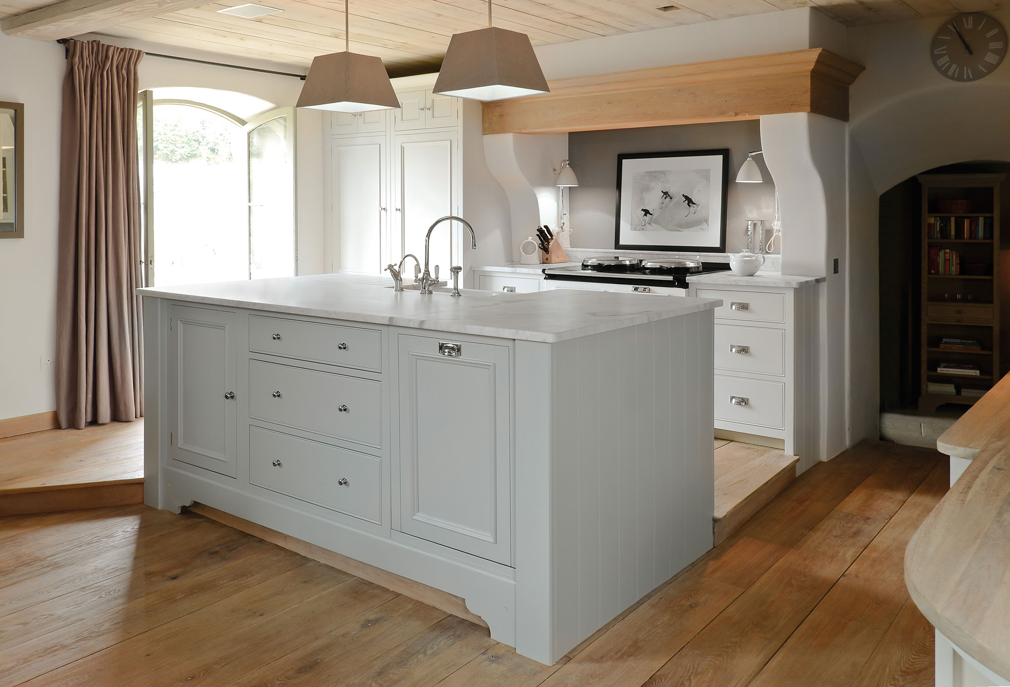 Moderne Landhausküche mit Kochinsel und Massivholzfußboden Helle Küche im Landhausstil mit großer Kochinsel, weißen Schränken, Holzboden und stilvoller Beleuchtung