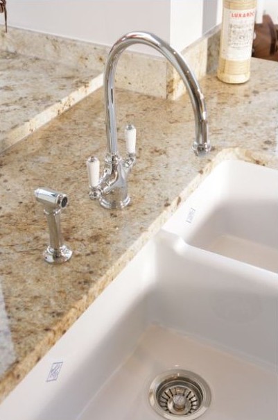 Moderne Spüle mit Doppelbecken und eleganter Armatur auf Granit-Arbeitsplatte Hochwertige Doppelspüle aus Keramik mit moderner Chromarmatur und Granit-Arbeitsplatte in einer Küche