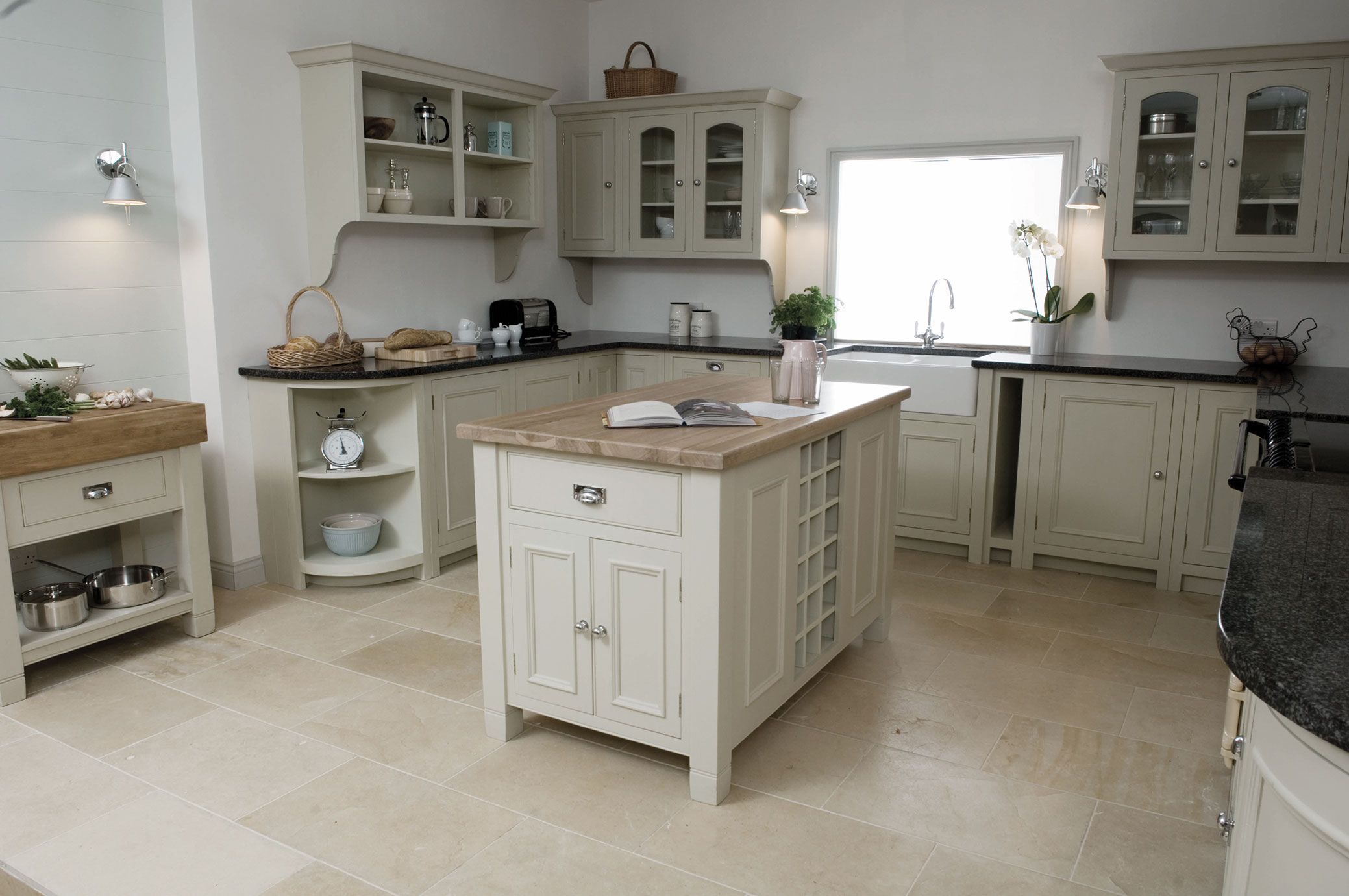 Moderne Landhausküche mit Kücheninsel und cremefarbenen Schränken Helle Landhausküche mit zentraler Kücheninsel, cremefarbenen Einbauschränken, Natursteinboden und großen Fenstern für viel Tageslicht.