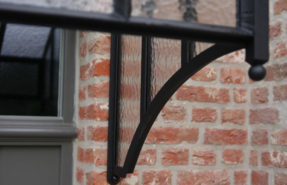 Detailansicht einer modernen Überdachung aus Glas und schwarzem Metall an einer roten Backsteinwand Glasüberdachung mit schwarzem Metallträger vor einer roten Backsteinwand, ideal als Wetterschutz für Türen oder Fenster