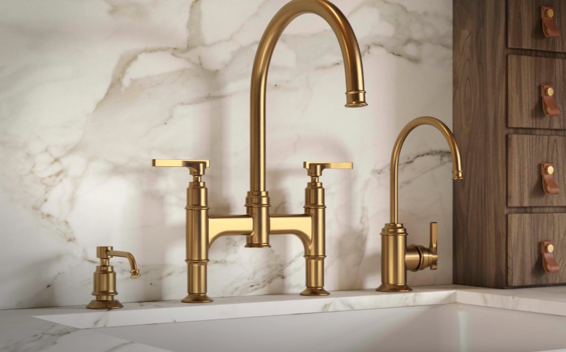 Luxuriöses Küchenarmaturen-Set aus Messing in Gold: hoher Schwanenhals, Zweihebel-Mischbatterie, separater Seifenspender und Zusatzhahn auf Marmorarbeitsplatte vor Marmorwand