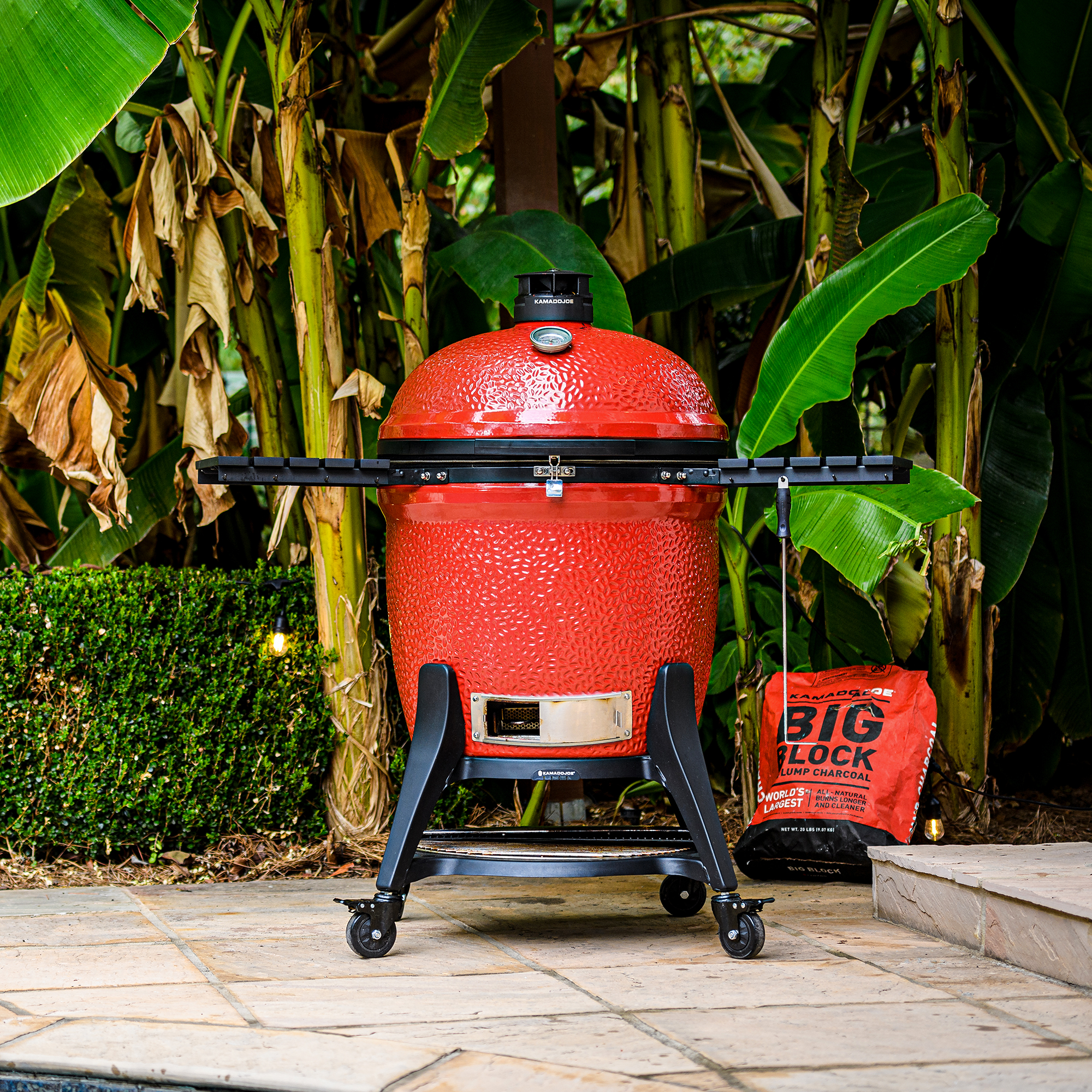 Kamado Joe Keramikgrill Classic II rot mit Rollwagen – Premium Grill für Garten und Terrasse Roter Kamado Joe Classic II Keramikgrill auf Rollwagen mit Ablagen, im Garten neben einem Sack Holzkohle