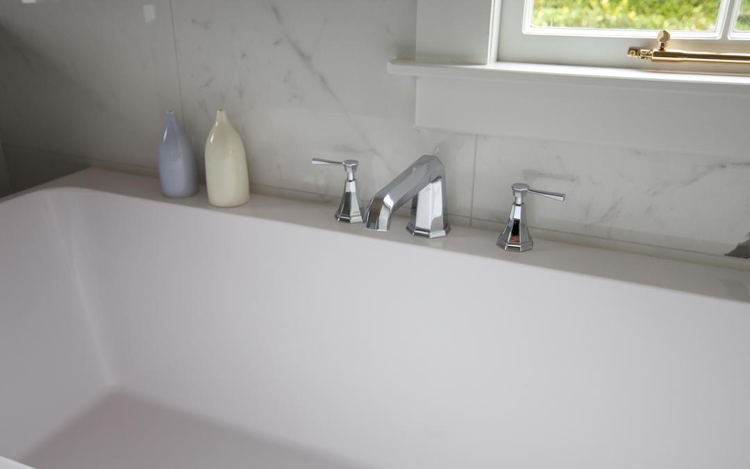 Weiße Badewanne mit 3-Loch-Wannenarmatur in poliertem Chrom, zwei Hebelgriffen und breitem Auslauf; modernes Design vor Marmorwand