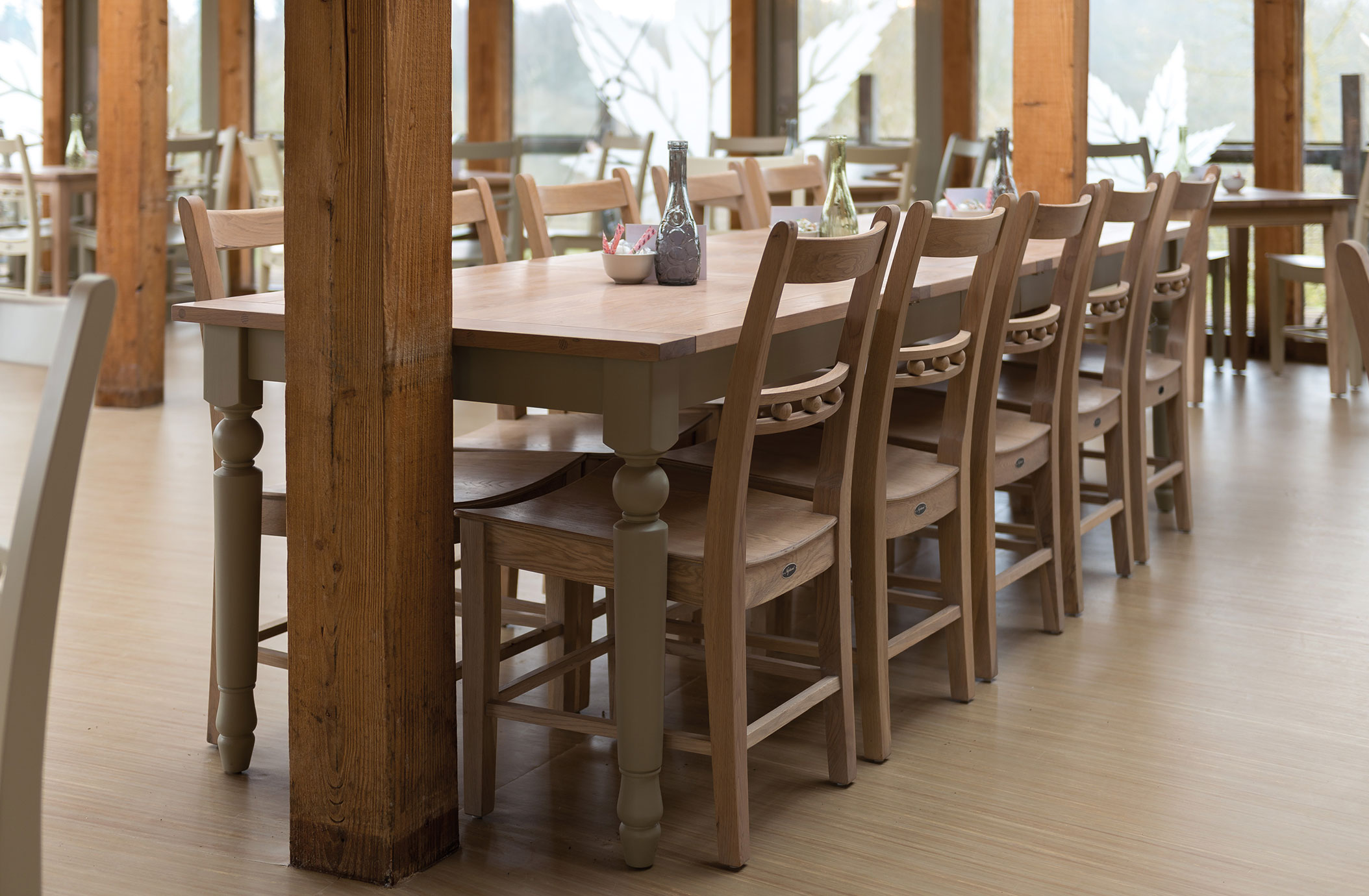 Großer Holztisch mit mehreren Stühlen in einem modernen, hellen Restaurant Langer Holztisch mit Holzstühlen in einem lichtdurchfluteten Restaurant mit natürlicher Einrichtung