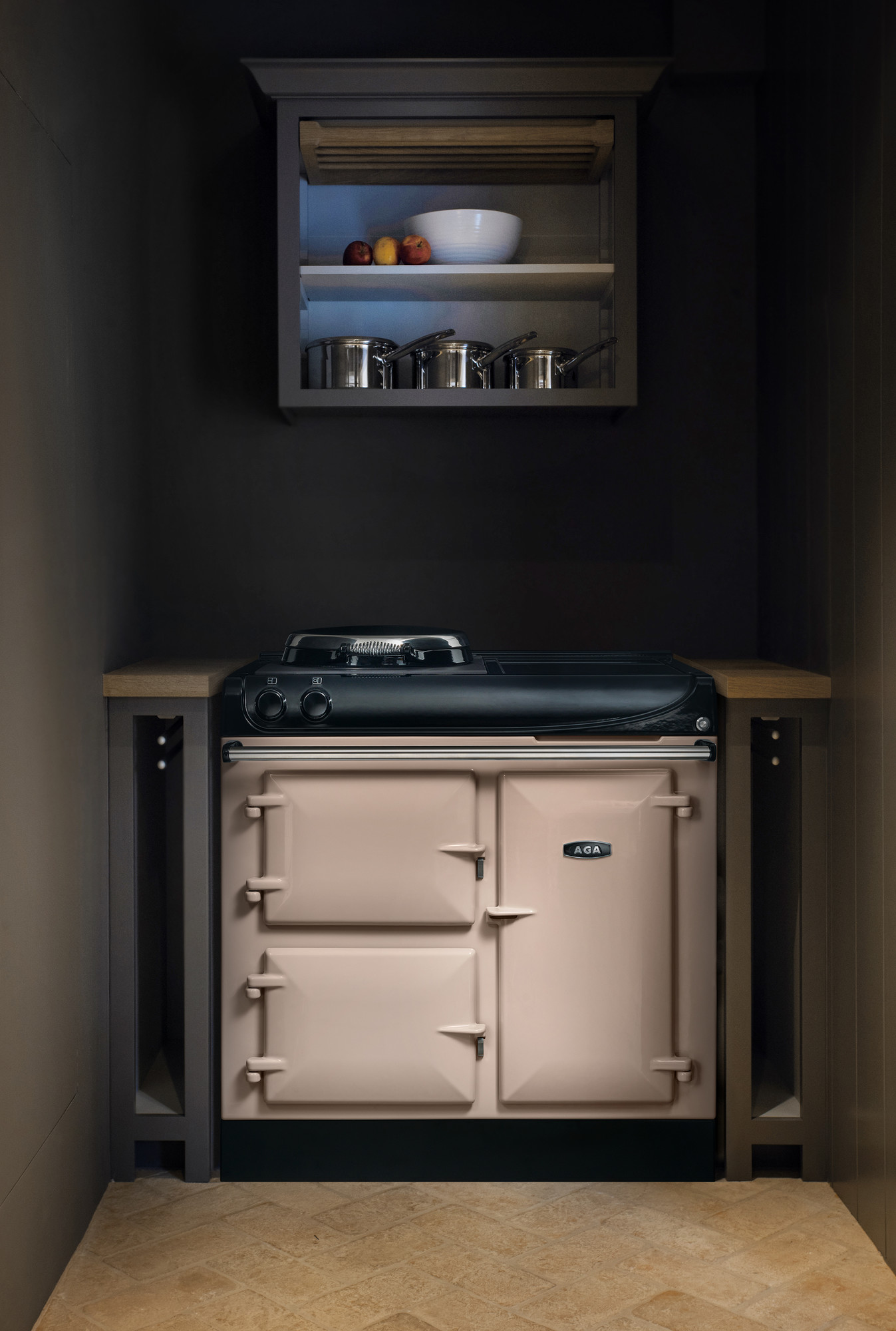 Beiger AGA Herd in moderner Küche mit Hängeschrank, Töpfen und Obstschale Stylischer, beiger AGA Herd in einer kleinen modernen Küche unter einem Hängeschrank mit Edelstahltöpfen, Schale und Äpfeln
