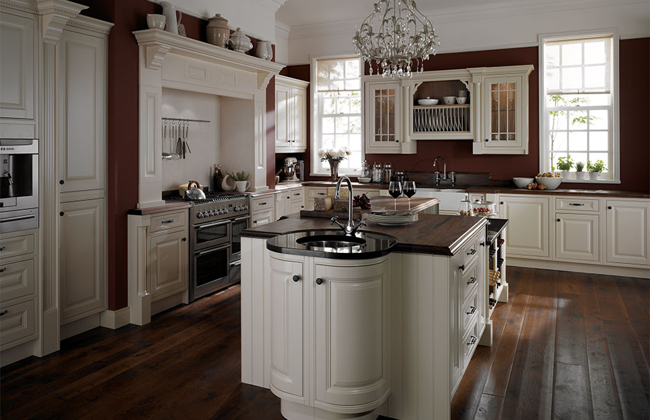 Elegante Landhausküche mit Kücheninsel, weißen Schränken und dunkler Arbeitsplatte Großzügige Landhausküche mit cremeweißen Fronten, Kochinsel, Kronleuchter und dunklem Holzboden