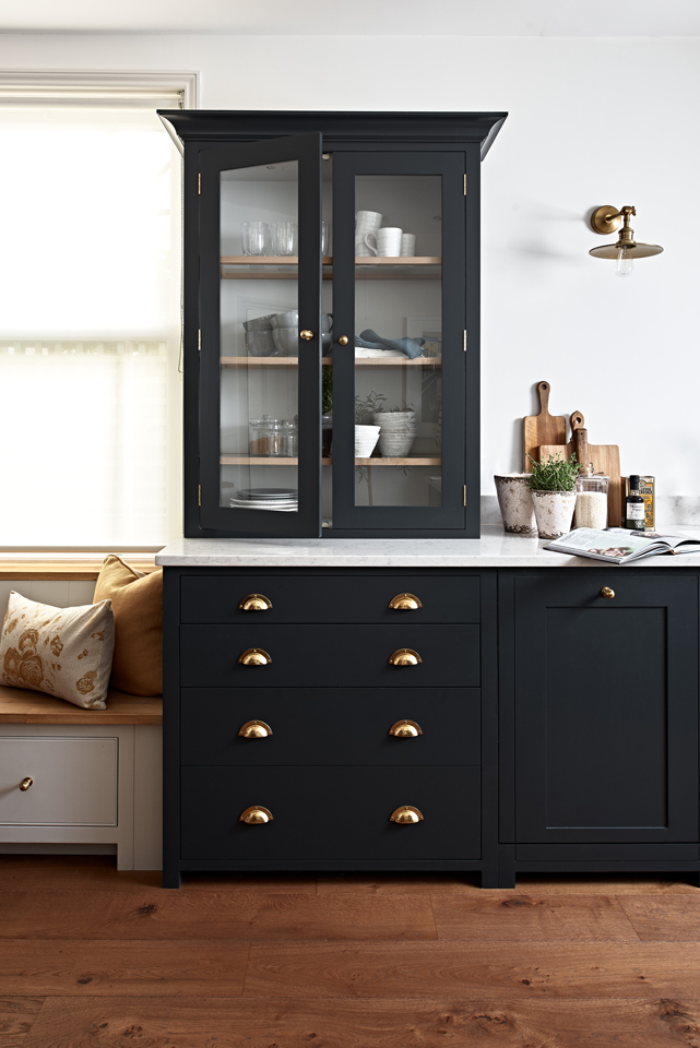 Eleganter Küchenschrank in Schwarz mit Glastüren, goldenen Griffen und Marmorarbeitsplatte Schwarzer Küchenschrank mit Glastüren, goldenen Griffen und weißer Marmorplatte, daneben Sitzbank und Dekoration