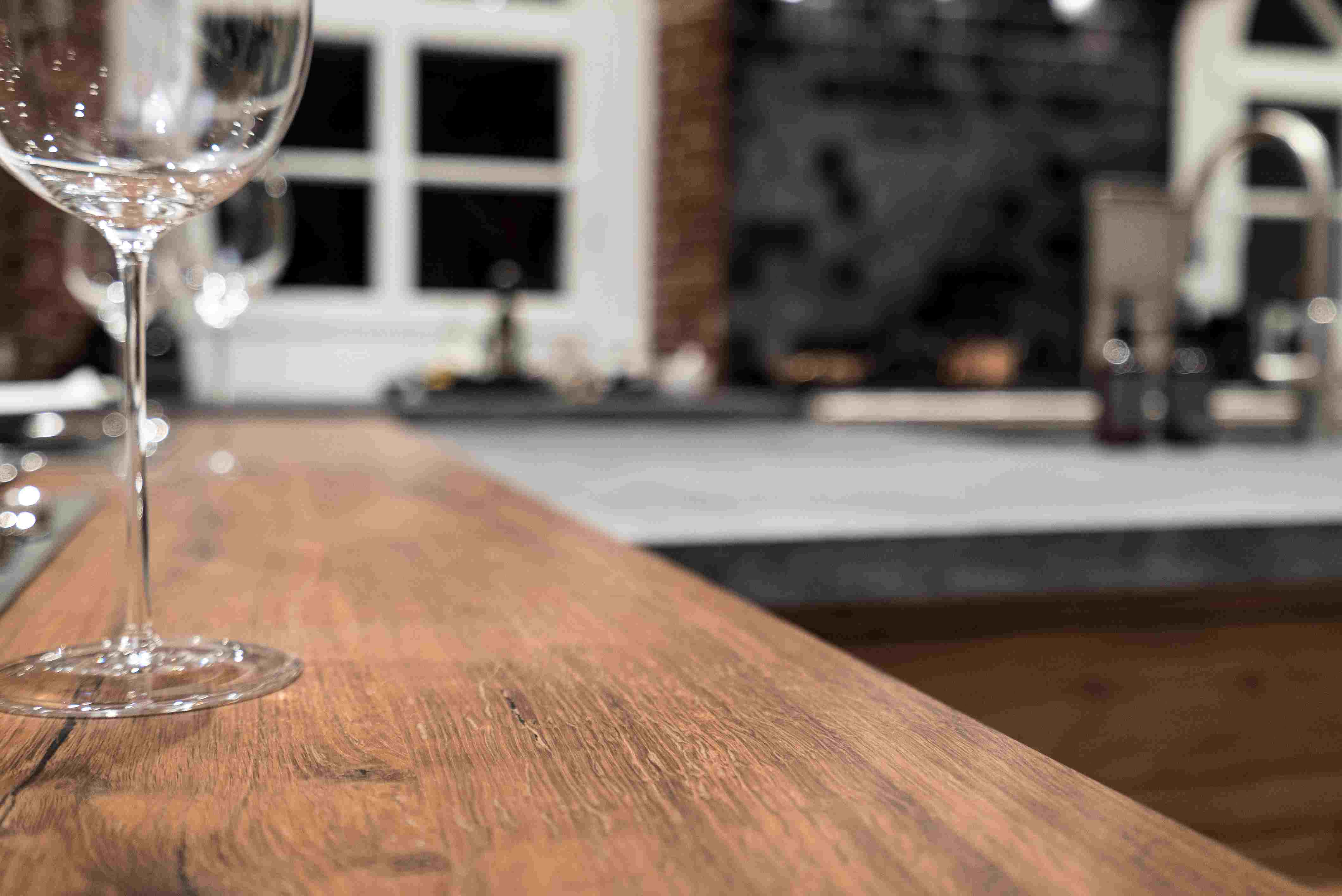 Nahaufnahme eines modernen Küchentresens aus Holz mit unscharfem Hintergrund und Weinglas im Vordergrund
