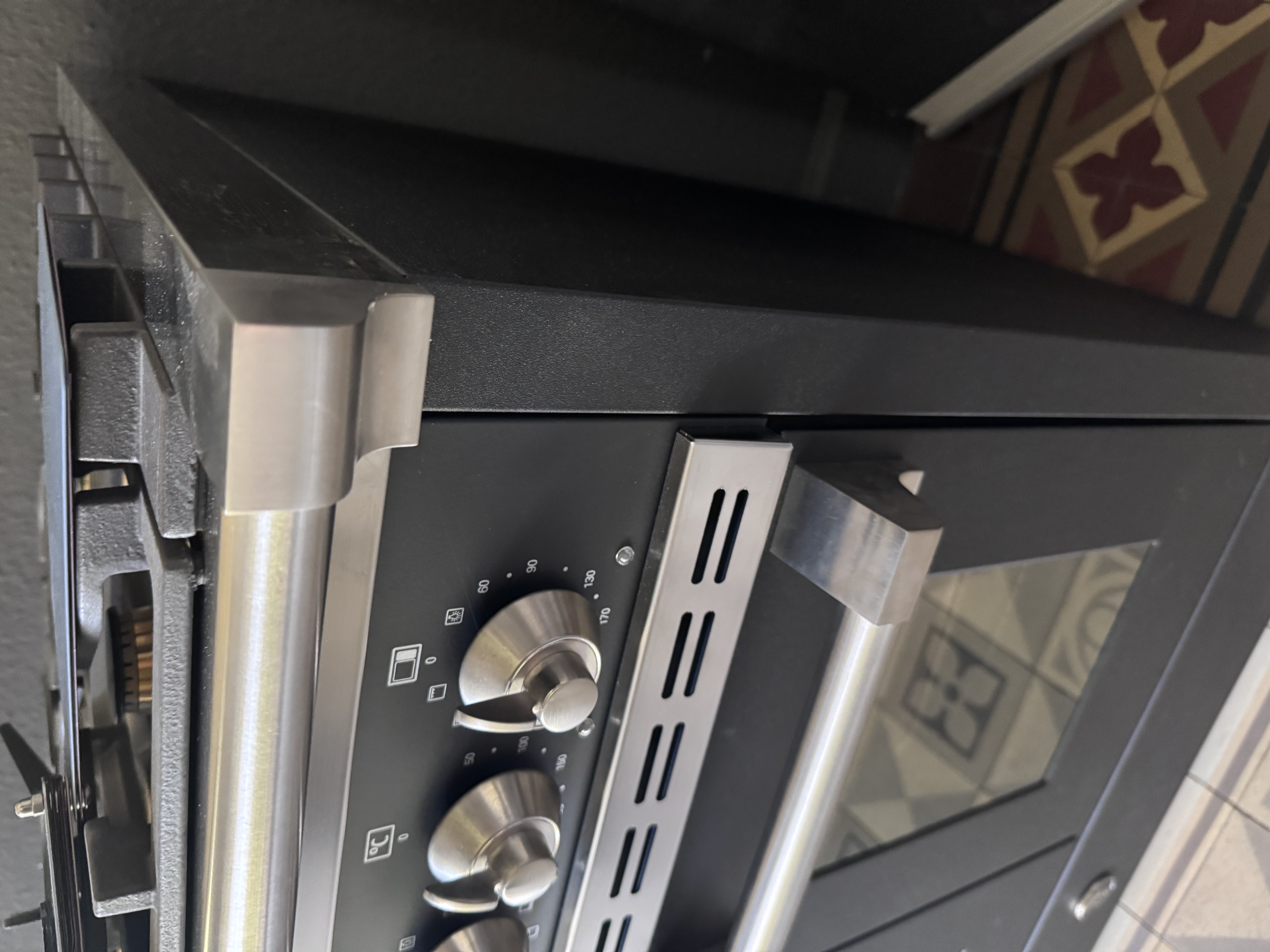 Nahaufnahme eines schwarzen Einbau-Backofens mit Edelstahlgriff, Drehknebeln, Temperaturskala und Glastür; modernes Küchengerät