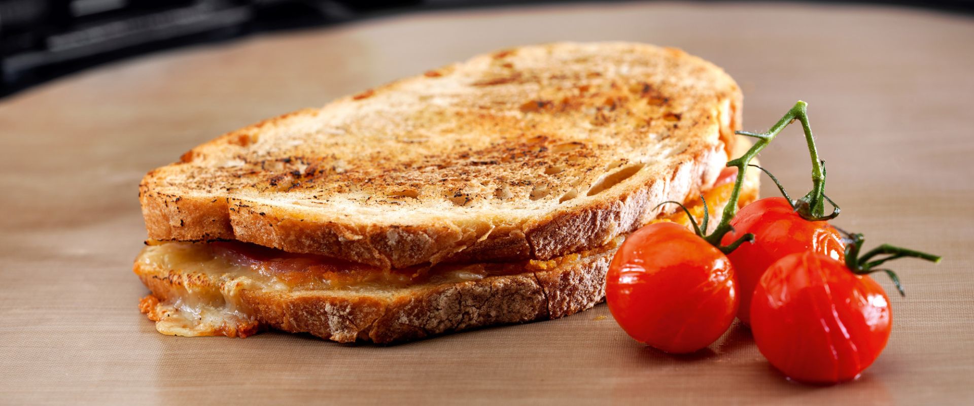 Goldbraun gegrilltes Käse-Sandwich mit geschmolzenem Käse neben frischen Rispentomaten – ideal zur Präsentation von Lebensmitteln, Sandwichmakern oder Grill- und Backzubehör