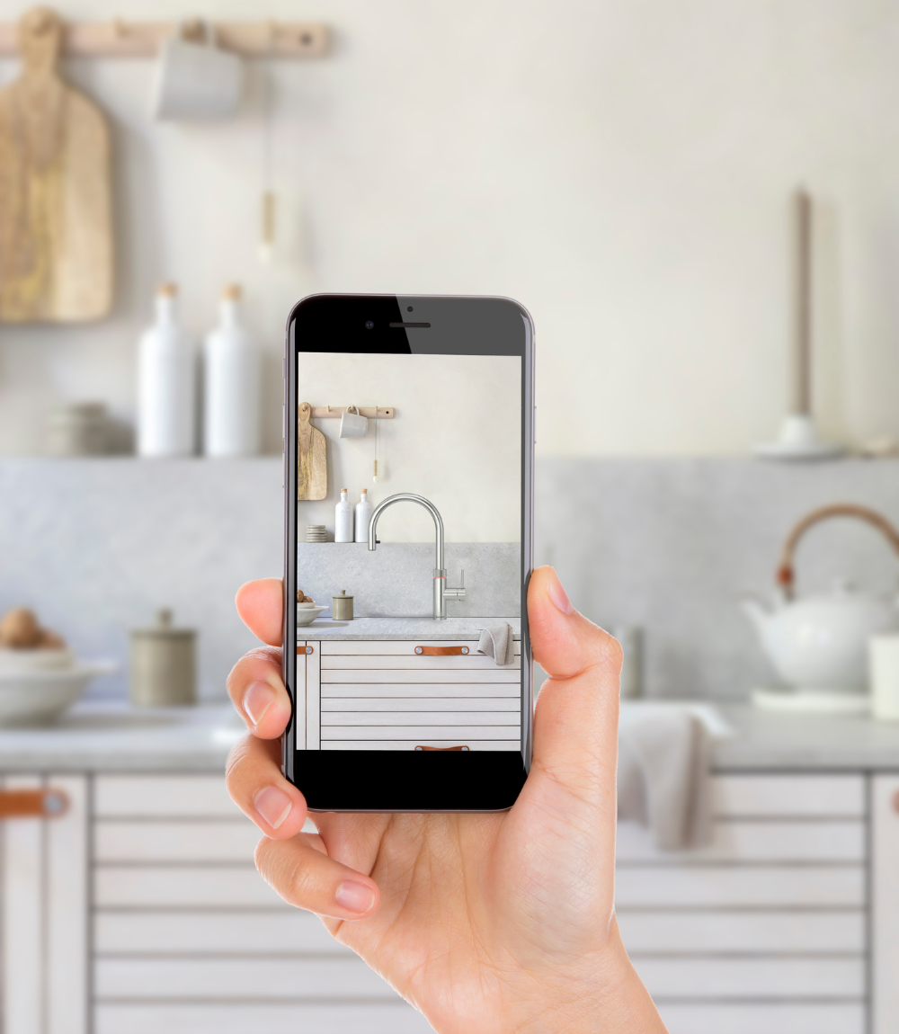 Hand hält Smartphone mit Foto einer modernen hellen Küche mit Wasserhahn Nahaufnahme einer Hand, die ein Smartphone hält, auf dessen Display eine moderne, minimalistische Küche mit Wasserhahn und hellen Holzelementen zu sehen ist