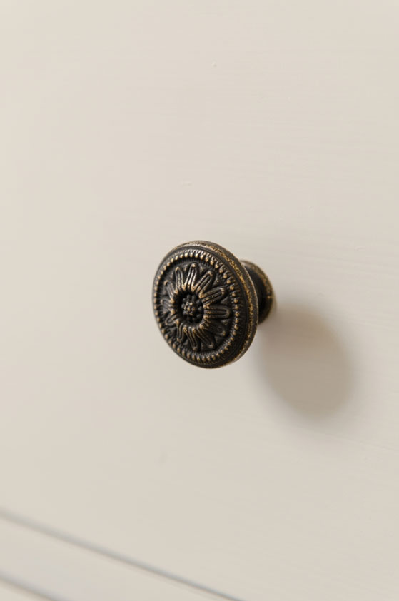 Dekorativer Möbelknopf aus Metall mit floralem Muster in Antik-Optik Detailaufnahme eines antik wirkenden, runden Möbelknaufs aus Metall mit floralem Muster an einer hellen Schublade