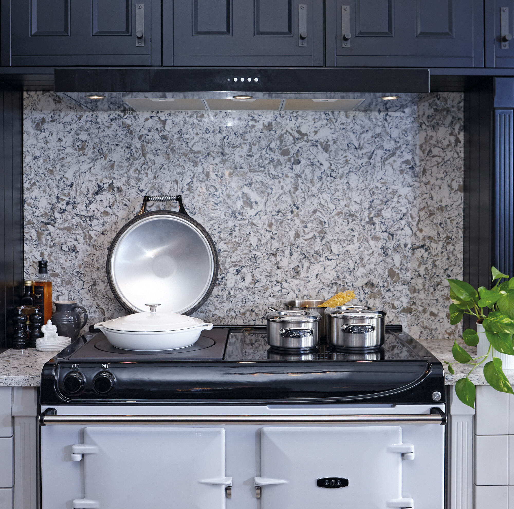 Küchenszene mit modernem Herd und Kochtöpfen aus Edelstahl vor grauer Steinspritzwand Moderner Herd mit weißen und Edelstahl-Kochtöpfen vor grauer Spritzschutzwand in stilvoller Küche