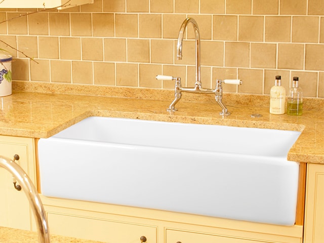 Große weiße Landhaus-Spüle aus Keramik mit moderner Armatur in einer Küche mit beiger Arbeitsplatte Landhausstil-Küchenspüle aus Keramik mit Armatur und beiger Naturstein-Arbeitsplatte