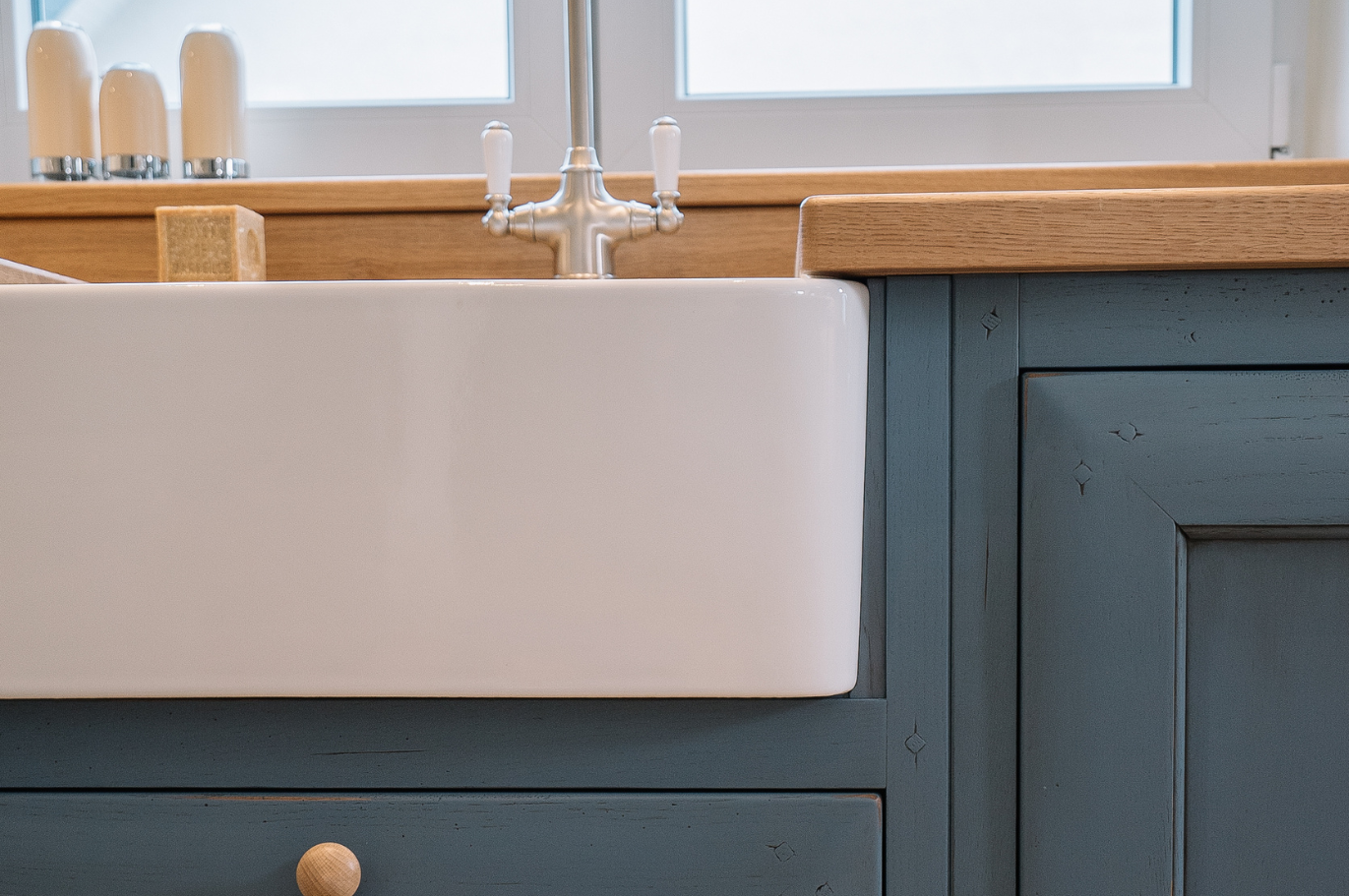 Landhausstil Spülbecken aus Keramik mit blauem Unterschrank und Holzarbeitsplatte Detailansicht eines weißen Keramikspülbeckens im Landhausstil mit blauem Holzunterschrank und Holzarbeitsplatte in einer hellen Küche