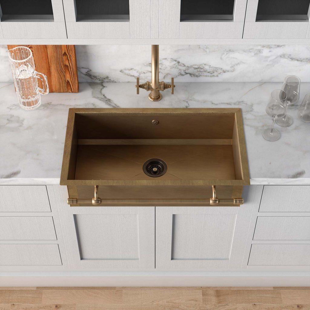 Oberansicht eines goldenen Messingspülbeckens mit moderner Armatur, eingebettet in eine weiße Küchenarbeitsplatte aus Marmor, umgeben von durchsichtigen Gläsern und einem Schneidebrett.