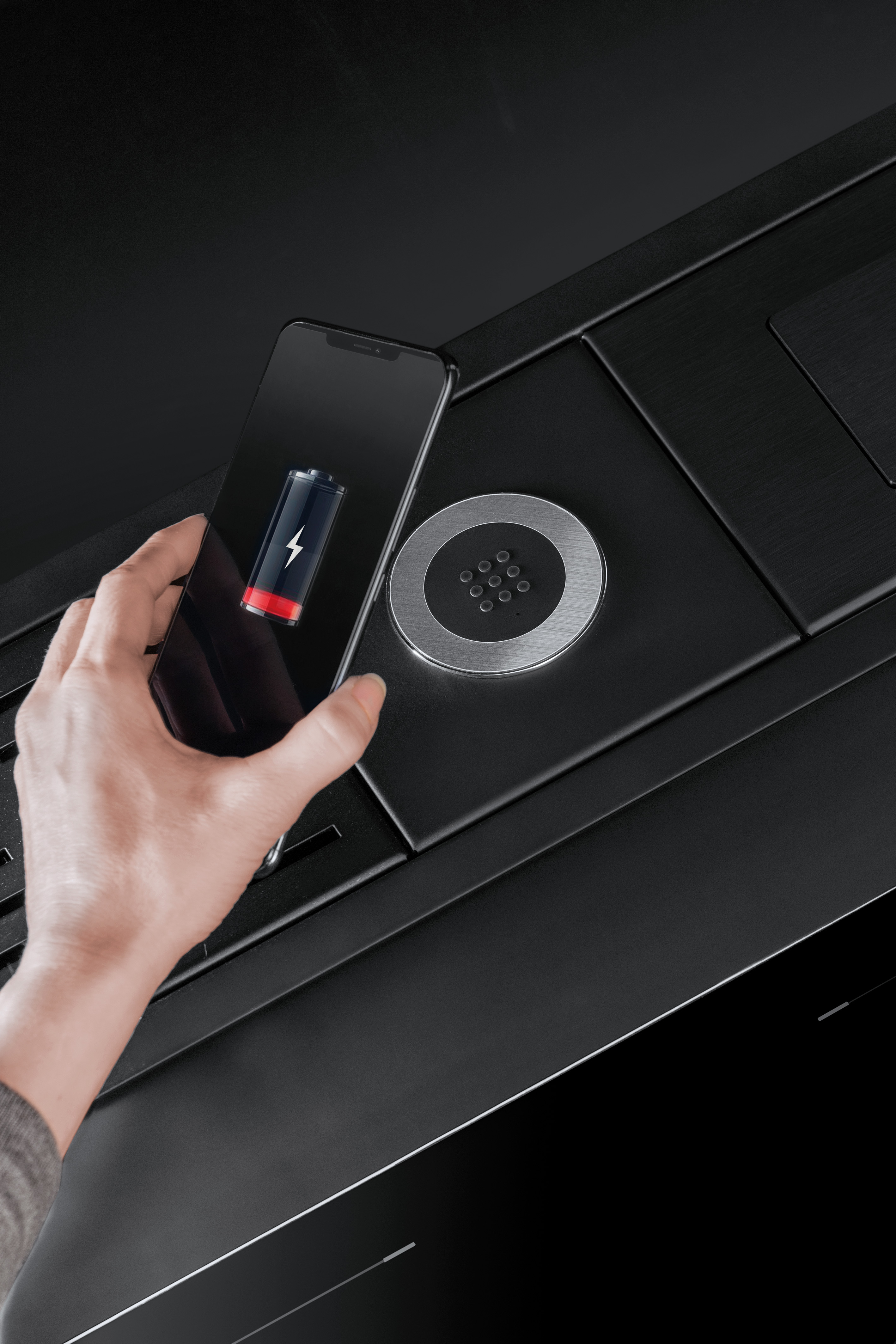 Smartphone wird per kabelloser Ladestation aufgeladen – moderne Qi-Ladetechnologie am Arbeitsplatz Hand hält ein Smartphone mit niedrigem Akkustand über eine kabellose Qi-Ladestation auf einem schwarzen Tisch