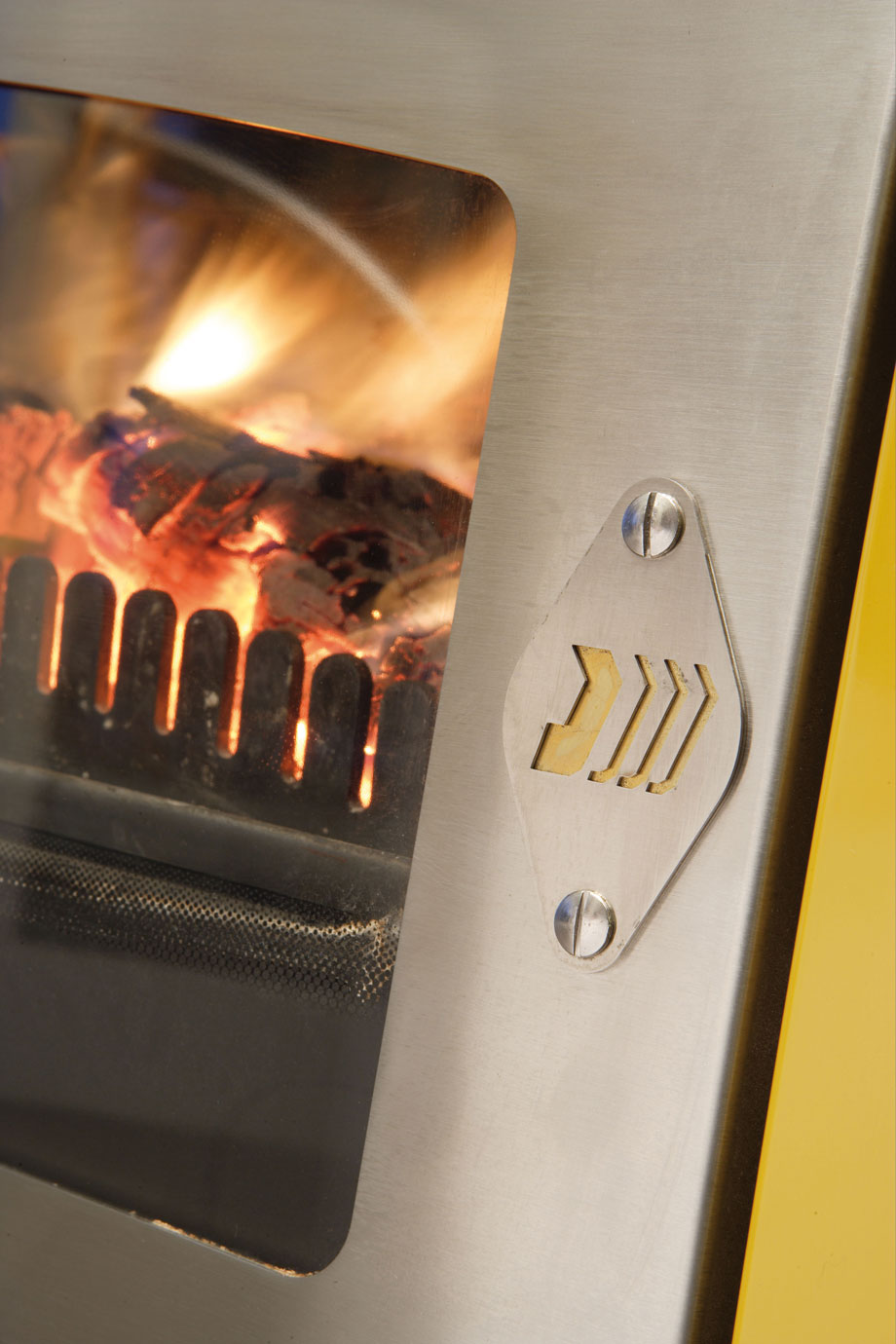 Detailansicht eines Holzofens mit Brennkammer und Flammen hinter einer Glasscheibe Nahaufnahme eines modernen Holzofens aus Edelstahl, Blick auf das Feuer durch die Glasscheibe und einen Lüftungsregler