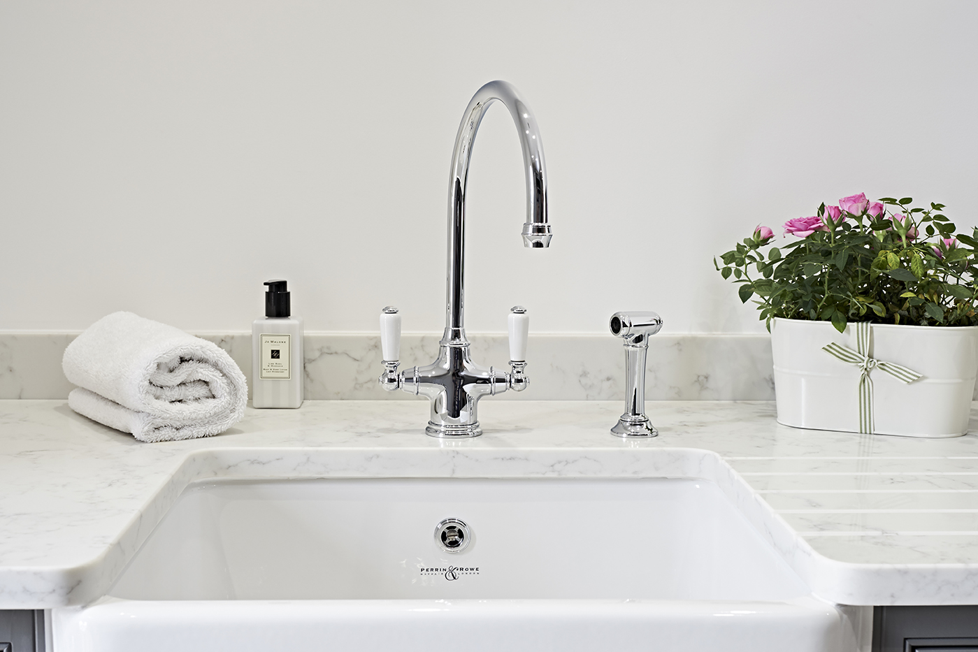 Elegantes Waschbecken mit modernem Wasserhahn, Handtuch, Seifenspender und Blumentopf auf Marmorarbeitsplatte Waschbecken aus Keramik mit glänzendem Chrom-Wasserhahn, weißem Handtuch, Seifenspender und Blumentopf mit rosa Blumen auf einer Marmorarbeitsplatte