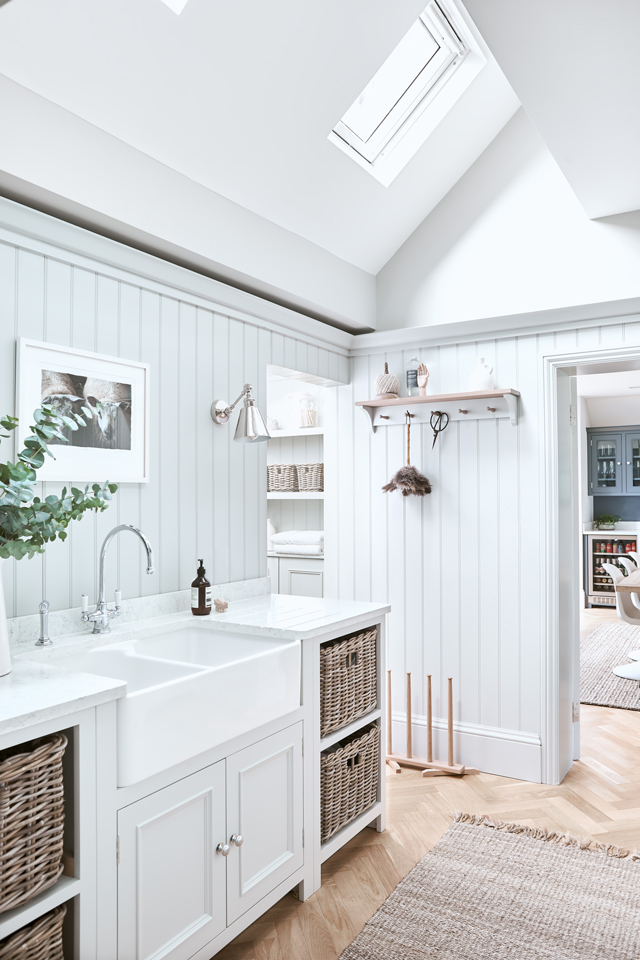 Heller Hauswirtschaftsraum mit großem Spülbecken, Korbregalen und Dachfenster im skandinavischen Stil Modern eingerichteter Hauswirtschaftsraum mit weißen Paneelwänden, Doppelspülbecken, geflochtenen Aufbewahrungskörben, Arbeitsplatte aus Marmor, Pflanzen und Tageslicht durch ein Dachfenster