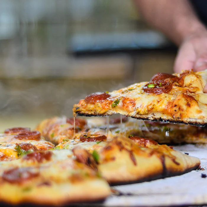 Frisch gebackene Pizza mit Salami und geschmolzenem Käse wird serviert Ein großes Stück heiße Pizza mit Salami und Käse wird aus einer ganzen Pizza gehoben. Die Pizza ist dampfend und der Käse zieht Fäden.