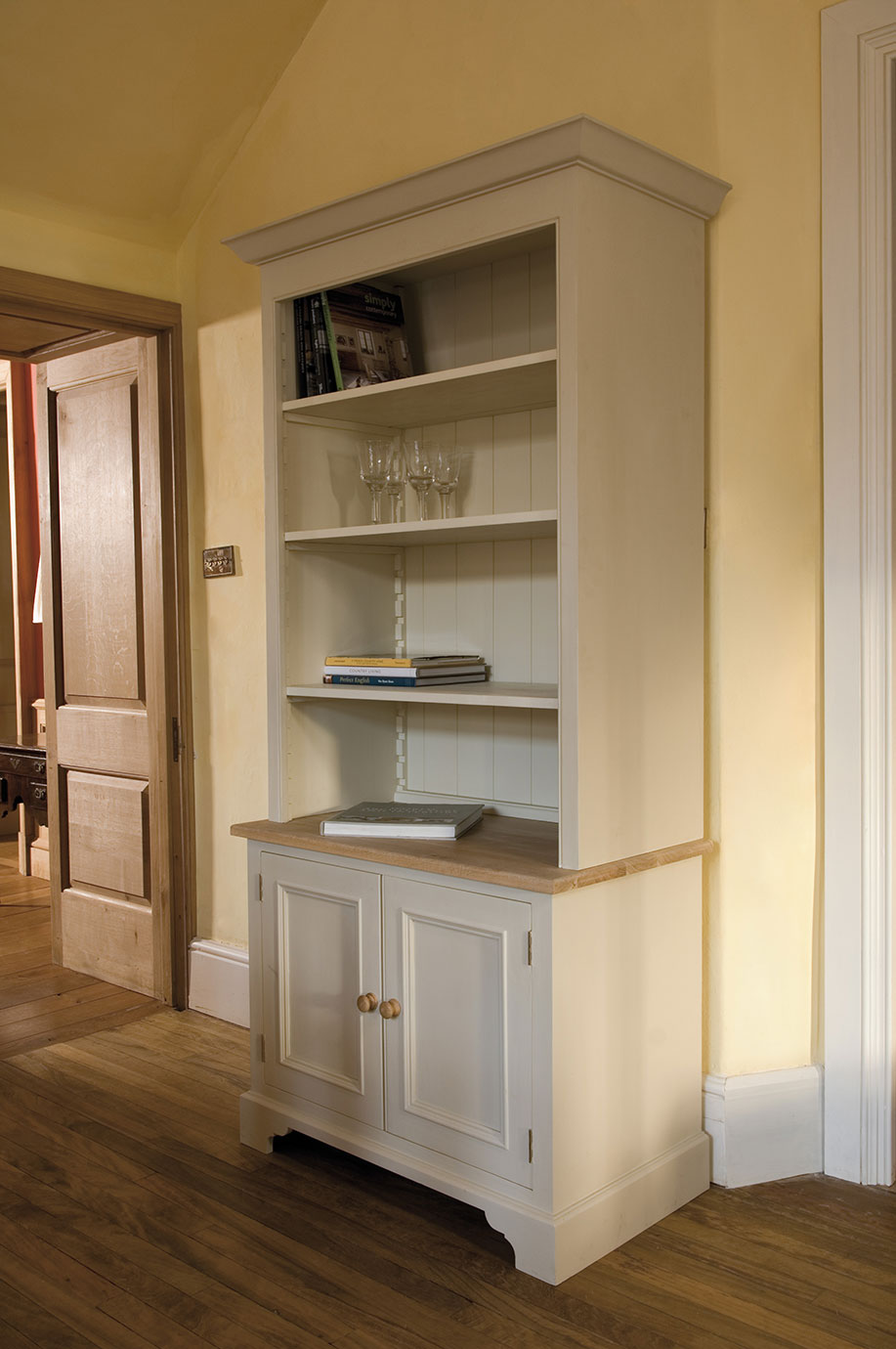 Landhausstil Buffetschrank aus Holz, cremefarben mit Ablage und Stauraum Cremfarbener Buffetschrank im Landhausstil mit offenen Regalen, Gläsern und Büchern, darunter Schranktüren und Holzplatte in einem gemütlichen Raum
