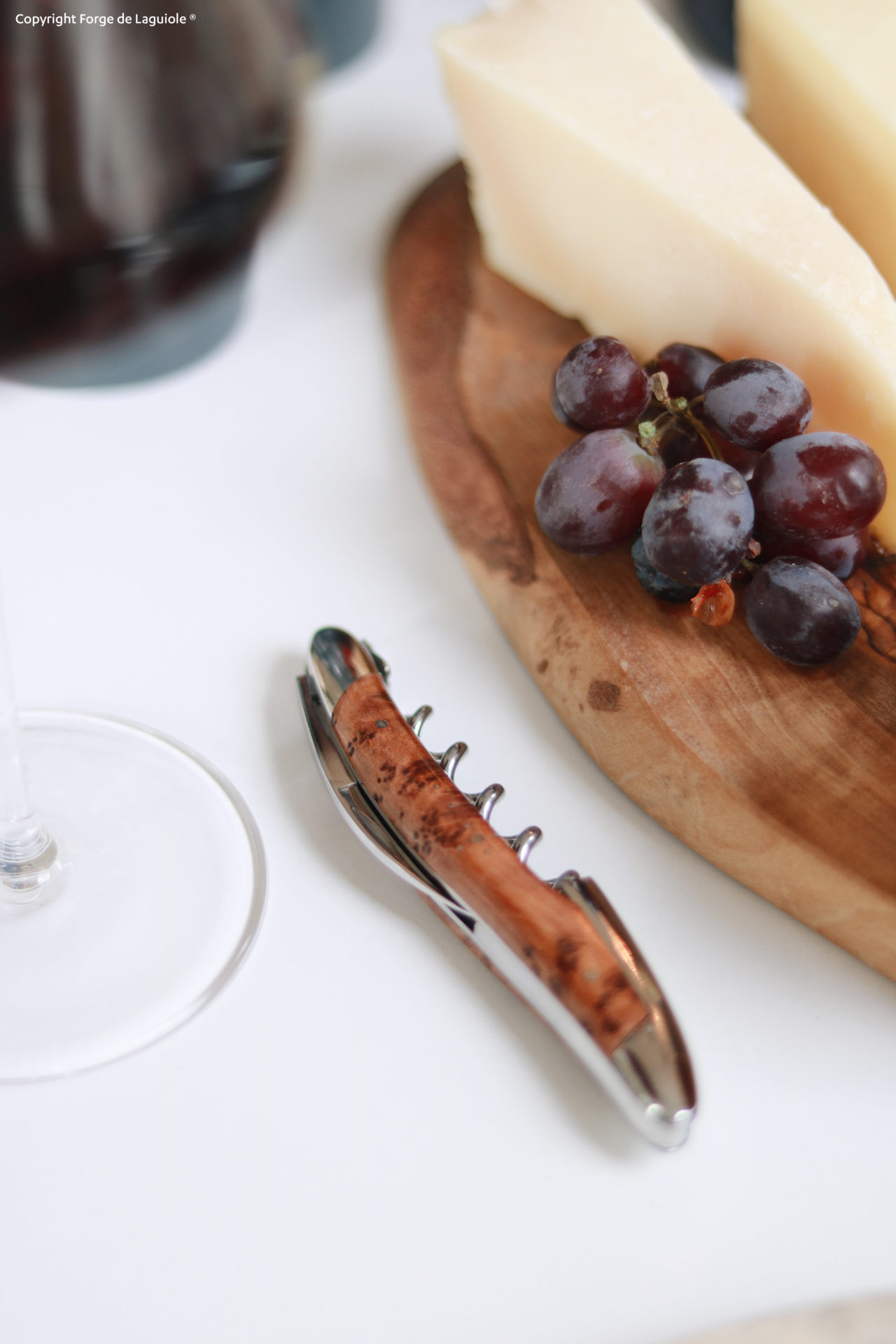 Edler Korkenzieher aus Holz neben Wein, Trauben und Käse auf Holzbrett Korkenzieher mit Holzgriff liegt auf einem Tisch neben einem Glas Wein, Trauben und Käsestücken auf einem Holzbrett