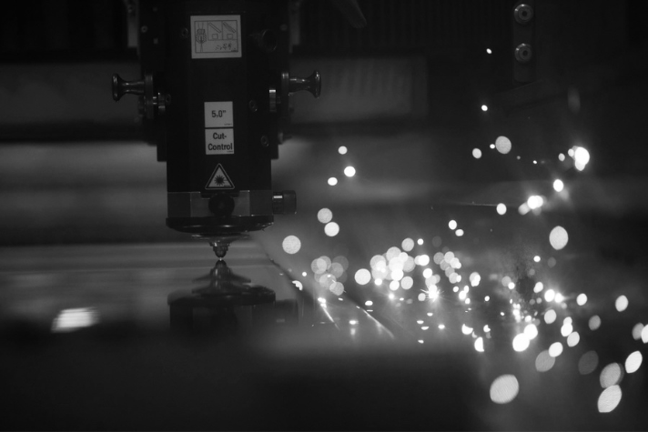 Industrielle Laserschneidmaschine beim Bearbeiten von Metall mit Funkenflug Eine Laserschneidmaschine schneidet Metall, während Funken entstehen, präziser Fertigungsprozess in Schwarzweiß