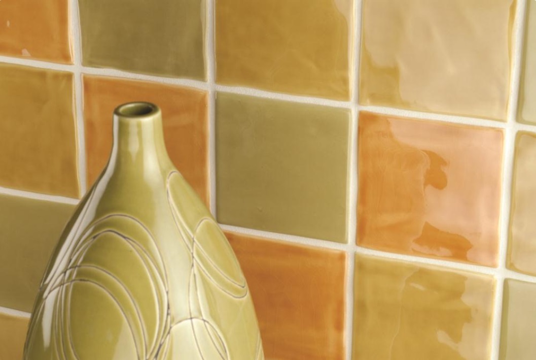 Keramikvase mit Muster steht vor einer Wand mit glänzenden Wandfliesen in verschiedenen Gelb- und Orangetönen.