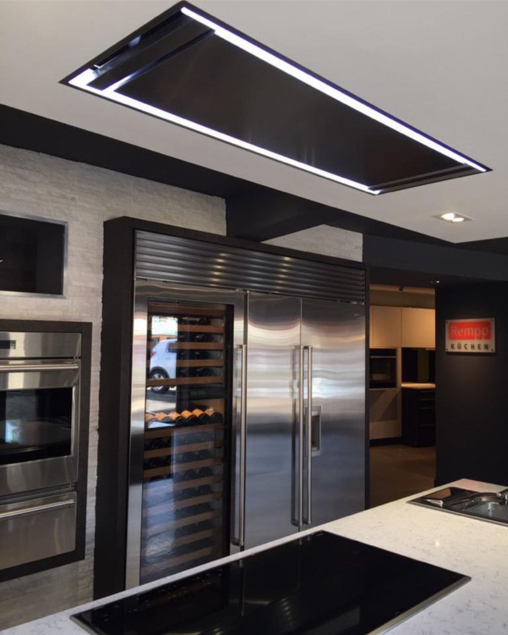 Moderne Einbauküche mit großer Dunstabzugshaube, Weinkühlschrank und Edelstahl-Kühlschrank Designerküche mit Decken-Dunstabzugshaube, Weinkühlschrank, Edelstahl-Kühlschrank und Kochinsel mit Induktionskochfeld