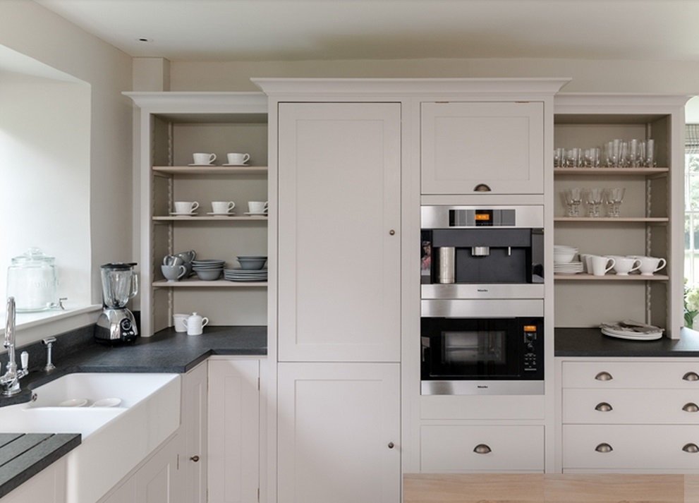 Moderne Einbauküche mit weißen Schränken, offenem Regal sowie Kaffeemaschine & Mikrowelle Helle Einbauküche mit weißen Fronten, offenen Regalen, Geschirr, Gläsern und integrierter Edelstahl-Kaffeemaschine und Mikrowelle