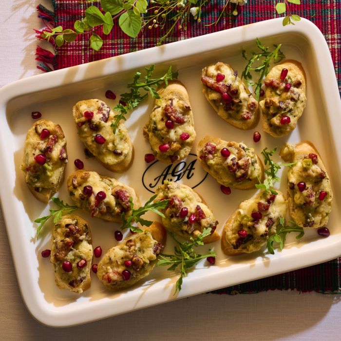 Ein weißes Tablett mit Bruschetta, belegt mit Käse, Granatapfelkernen und Rucola, auf einem festlichen Tisch