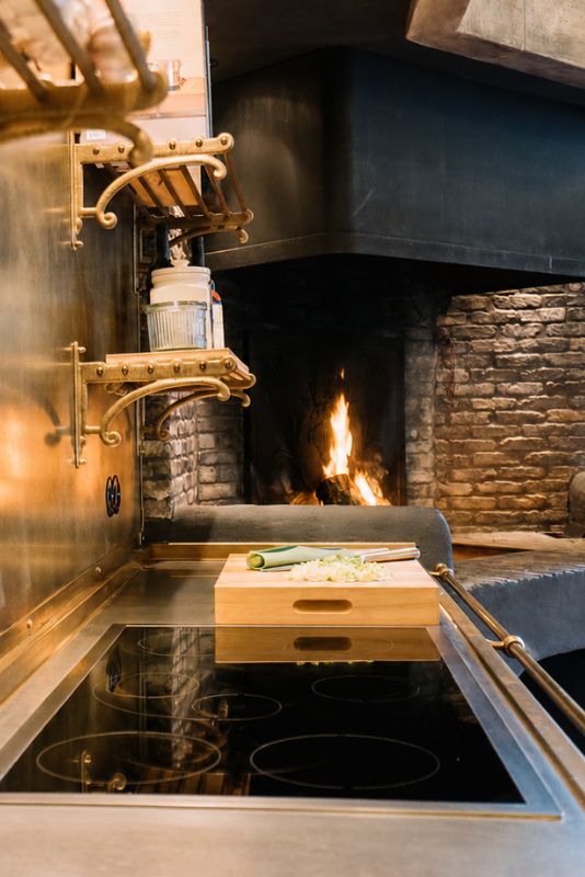 Modernes Induktionskochfeld mit schwarzer Glaskeramik, Holz-Schneidebrett und Kamin im Hintergrund – ideale Kochstelle für stilvolle Küchen