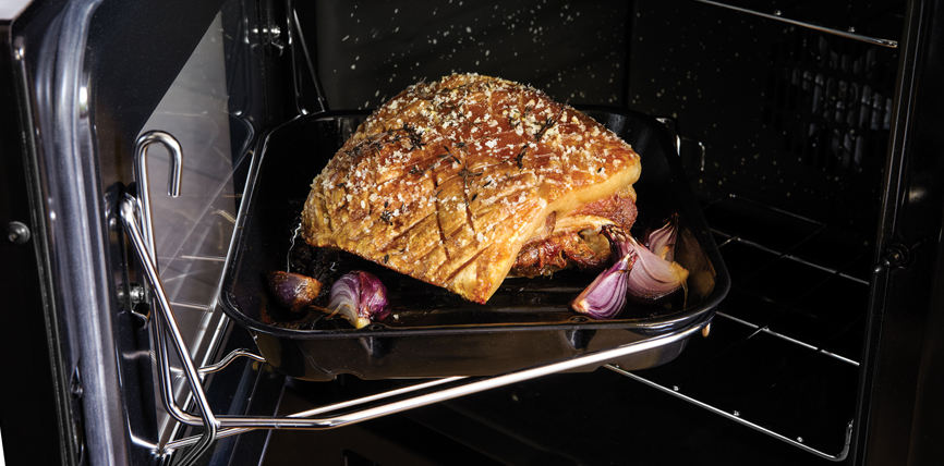 Knuspriger Schweinebraten mit Zwiebeln im Backofen auf Bratblech Ein knuspriger Schweinebraten mit Zwiebeln wird im Ofen auf einem Backblech zubereitet