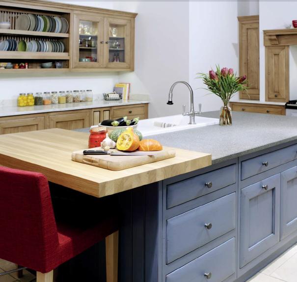 Moderne Landhausküche mit Kücheninsel, Spüle und Holzarbeitsfläche Große Kücheninsel mit grauen Schubladen, rotem Stuhl, Schneidebrett mit Gemüse, Spüle und Vase mit Blumen in einer modernen Landhausküche