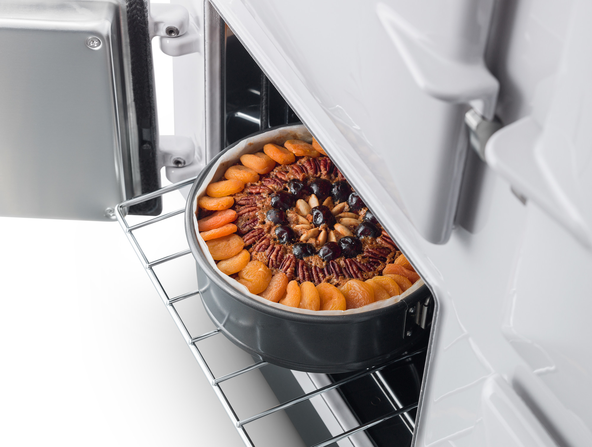 Kuchen mit getrockneten Aprikosen und Nüssen in einer Springform im geöffneten Backofen Frisch gebackener Kuchen mit Trockenfrüchten und Nüssen in einer runden Backform auf dem Backofenrost, Backofentür geöffnet