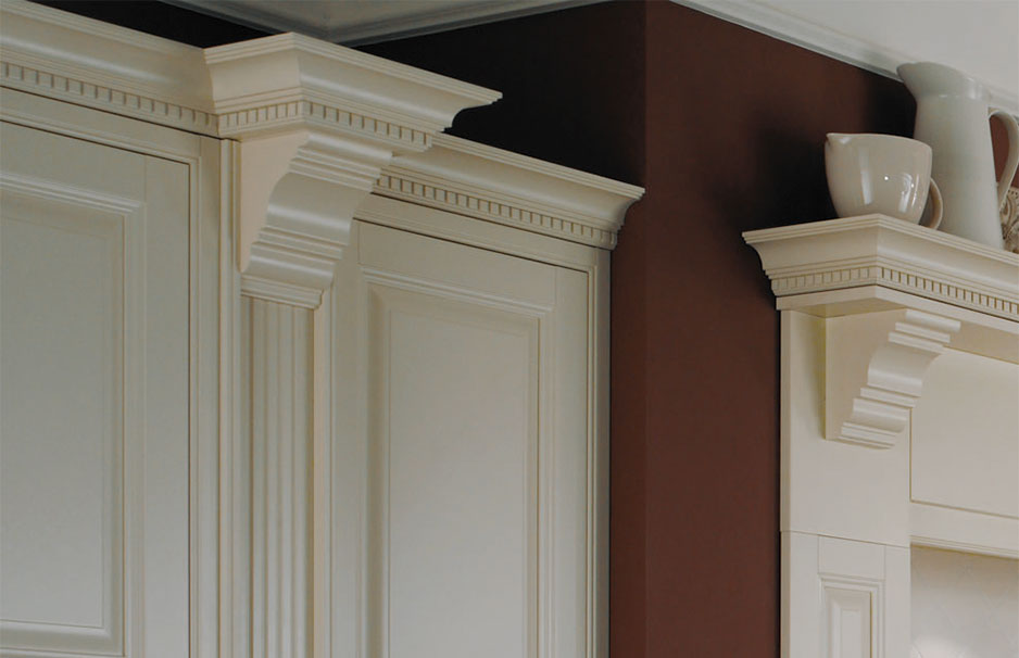 Küchenoberschränke in klassischem Design mit cremeweißen Zierleisten und dekorativen Kranzprofilen Detailansicht einer klassischen Küchenzeile mit cremeweißen Oberschränken, verzierten Leisten und dekorativen Kranzprofilen auf brauner Wand