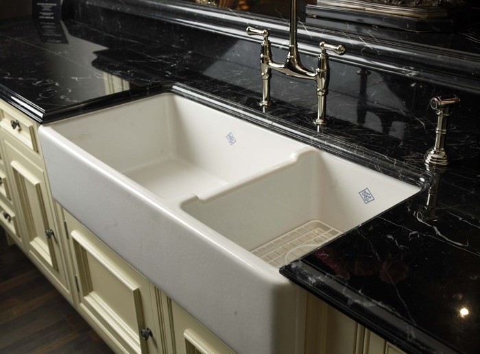 Doppelspülbecken aus Keramik mit schwarzer Marmorarbeitsplatte und klassischer Armatur in einer modernen Küche Weiße Keramik-Doppelspüle mit Markierung in einer schwarzen Marmorarbeitsplatte und eleganter Armatur in einer stilvollen Küche