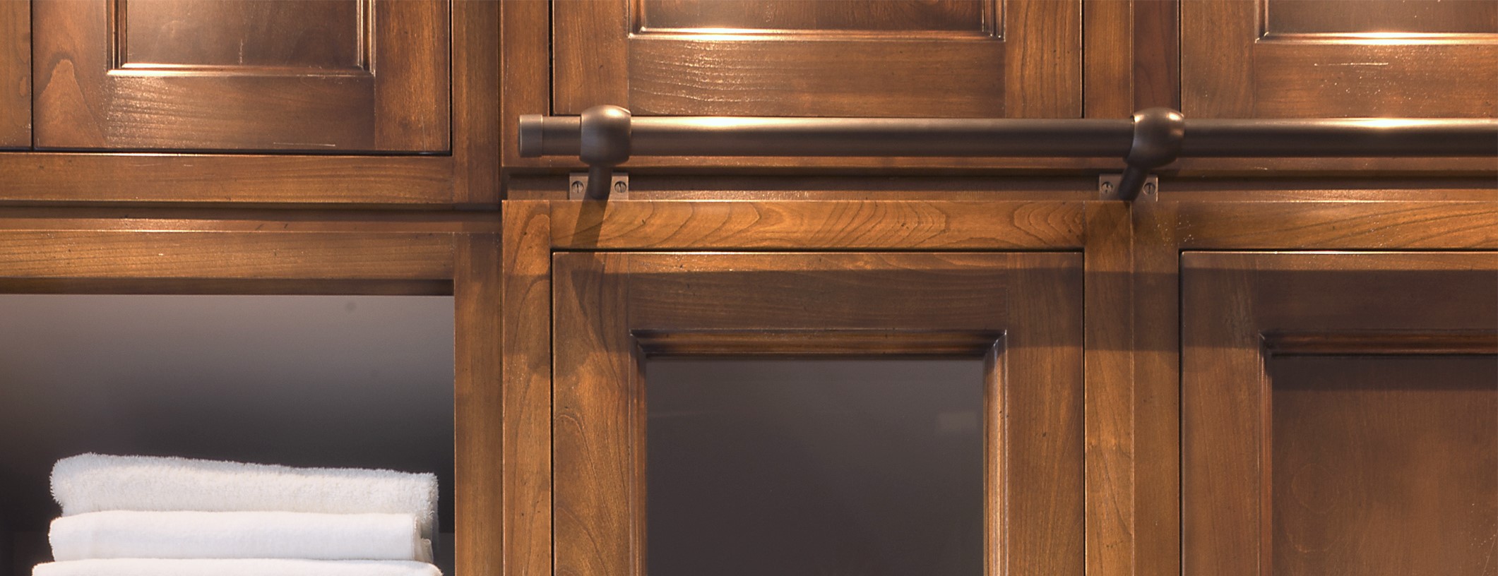 Hochwertiger Badezimmerschrank aus dunklem Holz mit schwarzen Metallgriffen Detailansicht eines Badezimmerschranks aus dunklem Holz mit modernen Griffen und weißen Handtüchern in einem offenen Fach