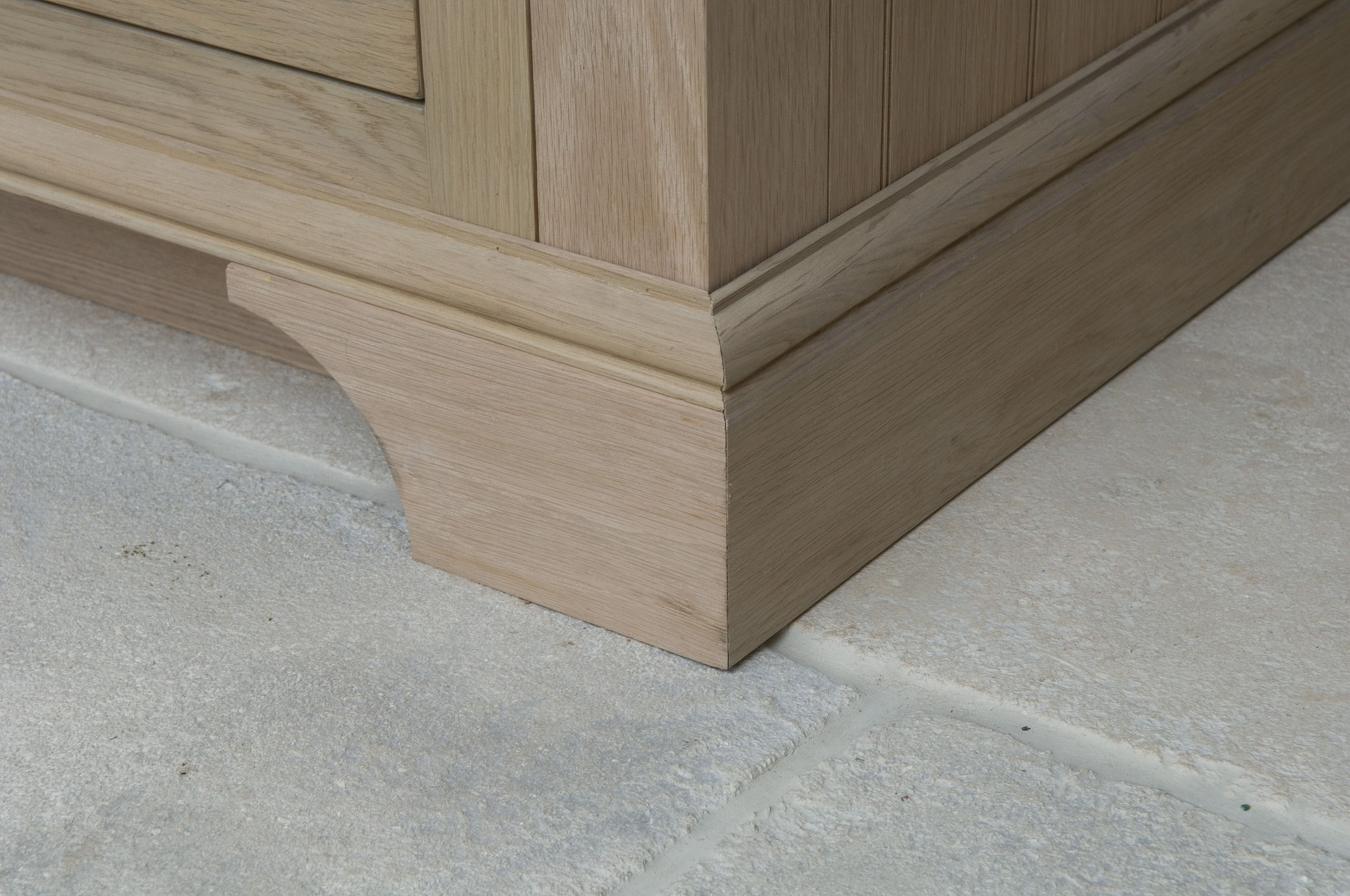 Detailansicht eines Massivholz-Sockels eines Möbelstücks auf Steinboden Nahaufnahme eines Sockels aus hellem Holz, Teil eines Möbelstücks, stehend auf hellem Steinboden