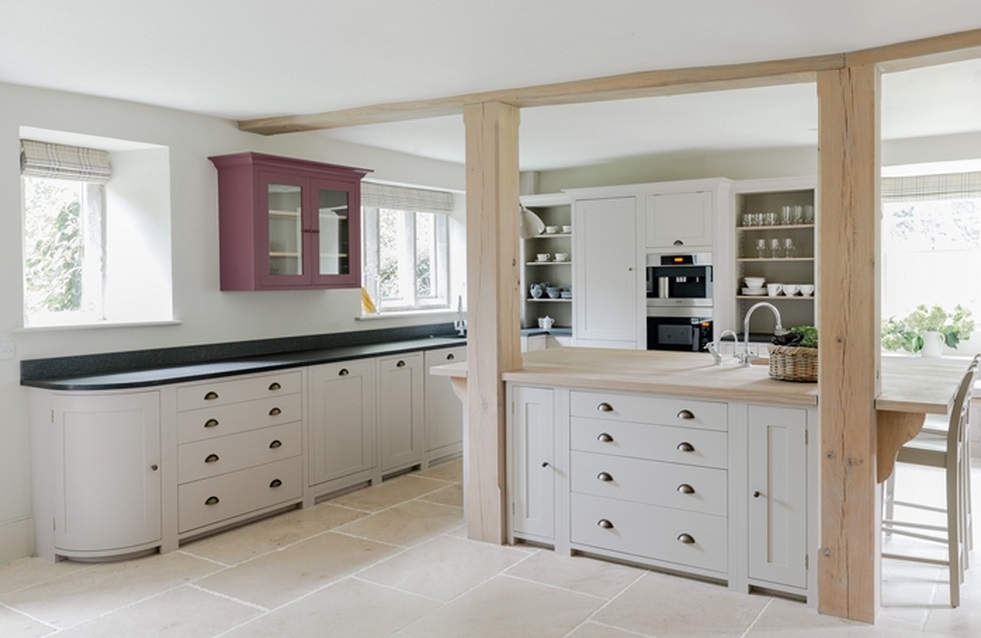 Moderne Landhausküche mit Kücheninsel, weißen Schränken und offenem Regalsystem Helle Küche im Landhausstil mit moderner Kücheninsel, weißen Einbauschränken, Holzarbeitsplatte und lila Hängeschrank