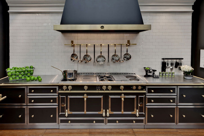 Luxuriöse Designerküche mit schwarzem Herd, Edelstahl-Arbeitsfläche und hängenden Töpfen Moderne Küche mit schwarzem Herd, Edelstahlarbeitsfläche, Küchenutensilien, Hängeregal und grünem Obstkorb