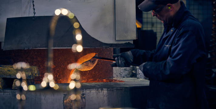 Metallarbeiter beim Einschmelzen von Metall in einer Werkstatt Ein Arbeiter in Schutzkleidung schmilzt Metall in einem Industrieofen