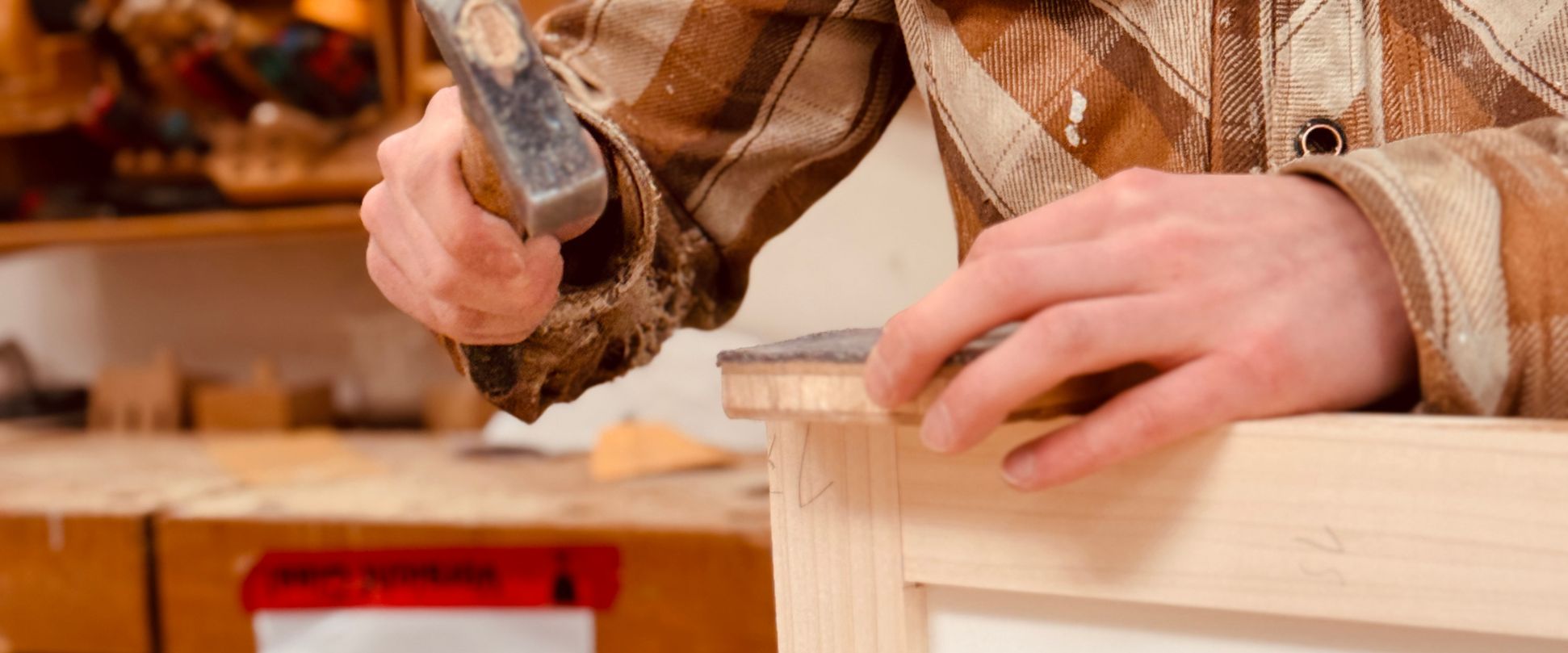 Nahaufnahme: Handwerker schlägt mit Hammer eine Verbindung an einem hellen Holzmöbel fest – detailgenaue Verarbeitung für langlebige Möbelstücke