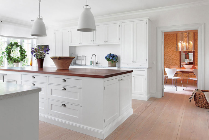 Moderne weiße Küche mit Kochinsel, Holzarbeitsplatte und eleganter Einrichtung Helle, moderne Küche mit weißen Schränken, großer Holzarbeitsplatte auf der Insel, Pflanzen, und Blick ins angrenzende Esszimmer