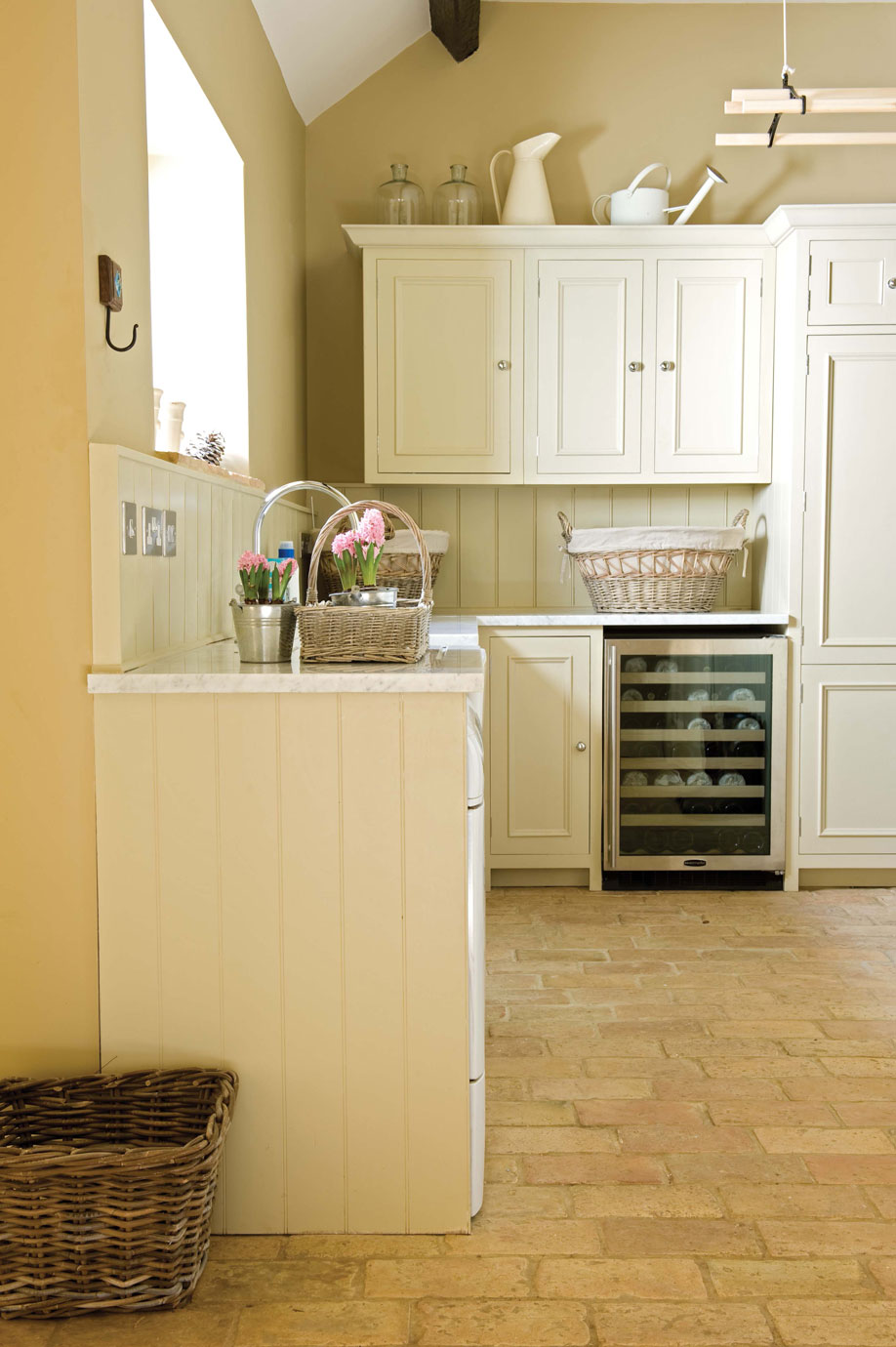 Helle Landhausküche mit cremefarbenen Schränken und Weinkühlschrank Gemütliche Landhausküche mit cremefarbenen Küchenschränken, Weinkühlschrank und dekorativen Körben mit Blumen auf der Arbeitsplatte