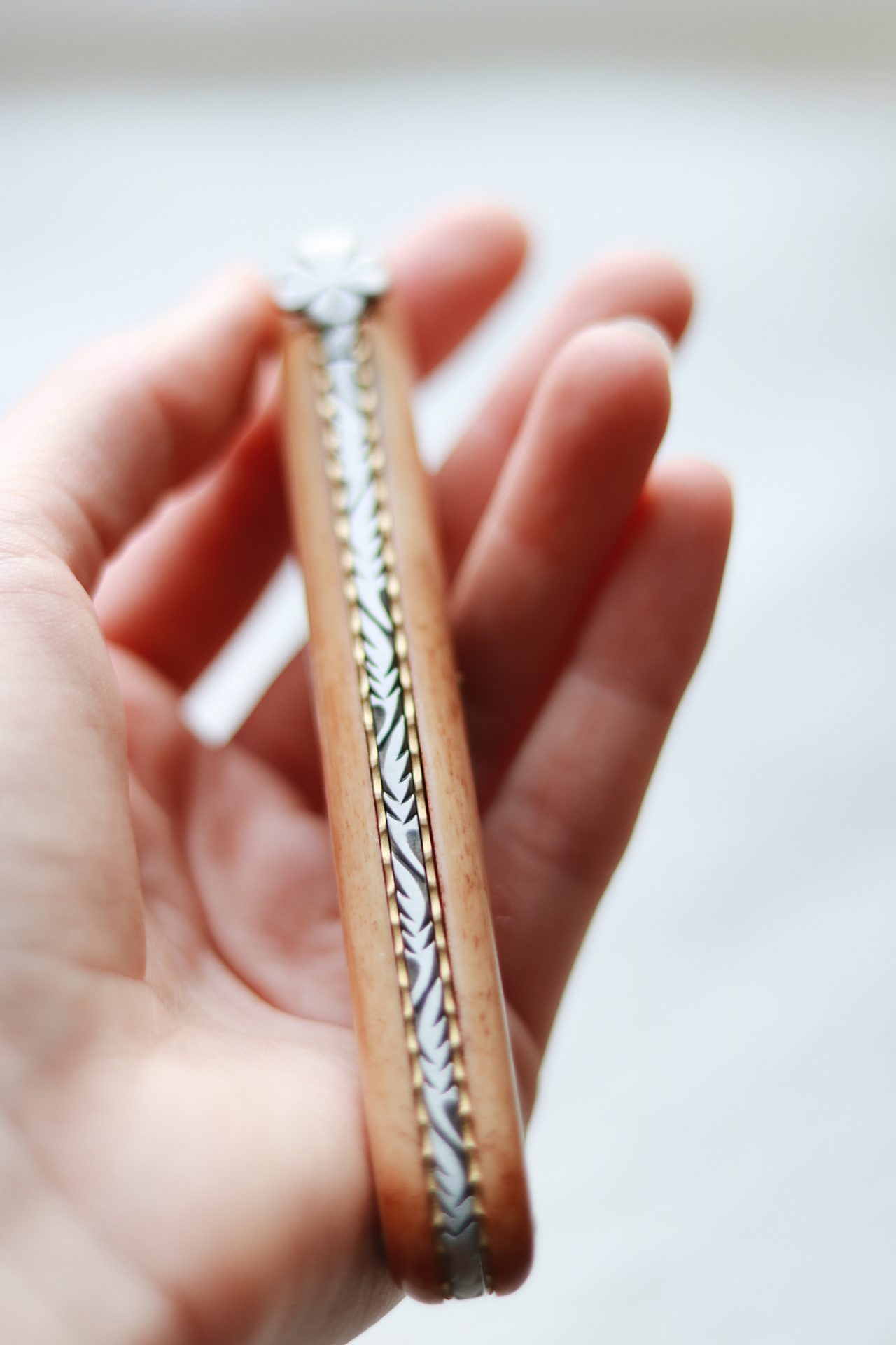 Detailaufnahme eines handgefertigten Taschenmessers mit verziertem Griff aus Holz und Metall Hand hält ein edles, handgefertigtes Taschenmesser mit kunstvoll gestaltetem Metallmuster am Holzgriff