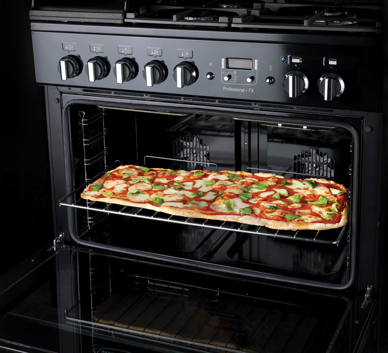 Geräumiger Backofen mit frisch gebackener rechteckiger Pizza auf dem Rost Offener Backofen mit einer großen rechteckigen Pizza mit Tomaten, Mozzarella und frischem Basilikum auf dem Rost